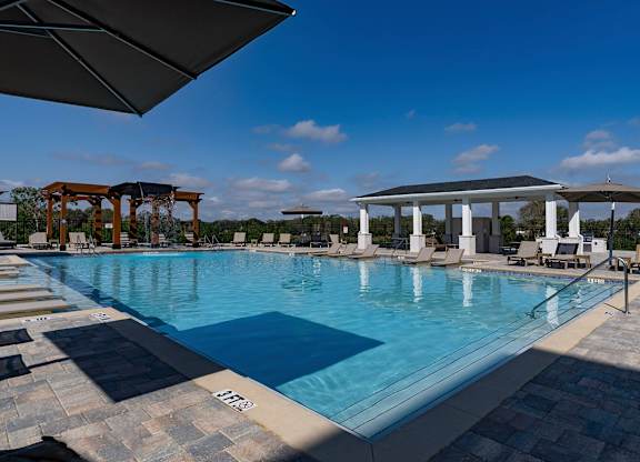 A large outdoor swimming pool with a tiled edge and a shaded area with lounge chairs at The Waverly at Winter Haven Apartments, Winter Haven, 33884