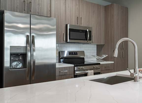 A modern kitchen with a stainless steel refrigerator, microwave, and oven at The Waverly at Winter Haven Apartments, Florida, 33884