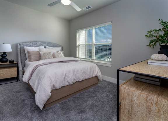 A bedroom with a large bed, a nightstand with a lamp, and a window with blinds at The Waverly at Winter Haven Apartments, Florida, 33884