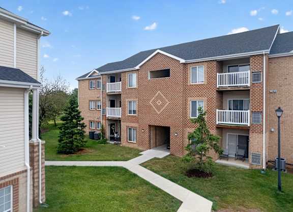 A brick apartment building with a balcony and a small tree in front.