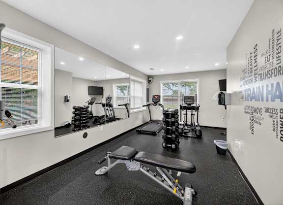 A gym room with a variety of equipment including weights and a bench.