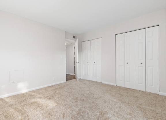 A room with white walls and carpeted floor with a doorway leading to another room.