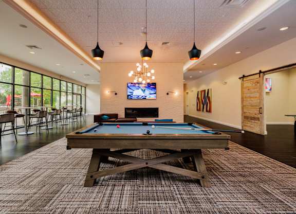 A billiards table with a blue cloth is in the middle of a room with a television and a pool table.