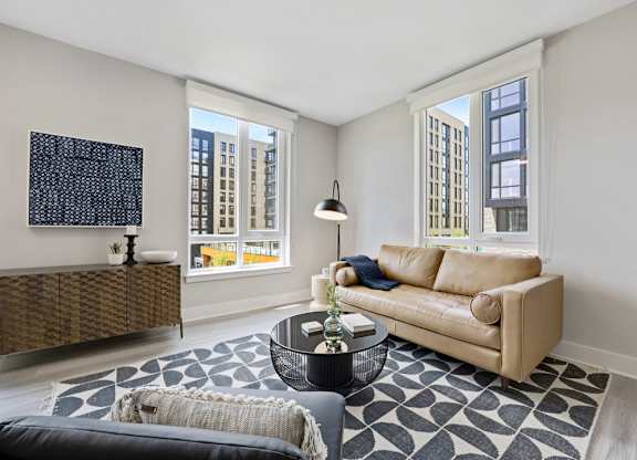 A living room with a tan couch and a black and white rug.