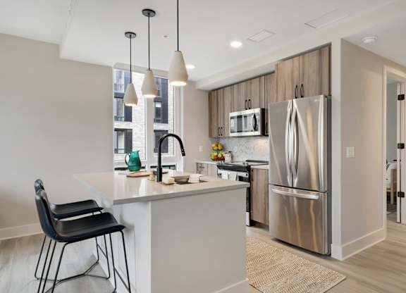 A kitchen with a refrigerator, microwave, and a counter with a chair.