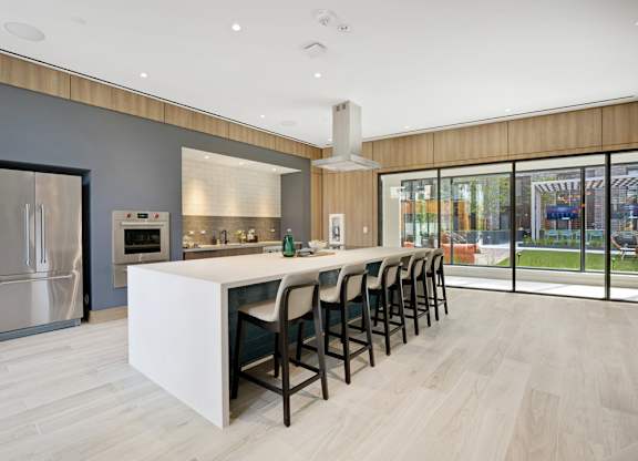 A modern kitchen with a long white island and black barstools.