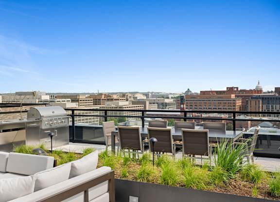 A rooftop patio with chairs and a table overlooking a cityscape.