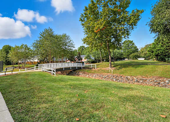 A park with a bridge, trees, and a clear sky.