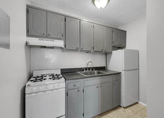 A kitchen with a white stove, sink, and cabinets.