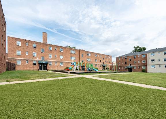 A playground in the middle of a grassy courtyard surrounded by brick buildings.