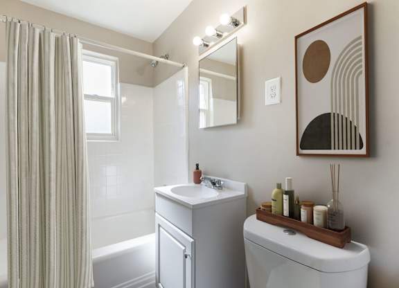 A bathroom with a white toilet, a white sink, a white bathtub, a mirror, and a picture on the wall.