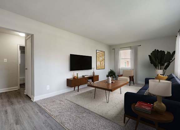 A living room with a blue couch, a wooden coffee table, and a flat-screen TV mounted on the wall.
