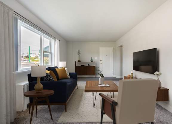 A living room with a blue couch, a wooden coffee table, and a flat screen TV mounted on the wall.