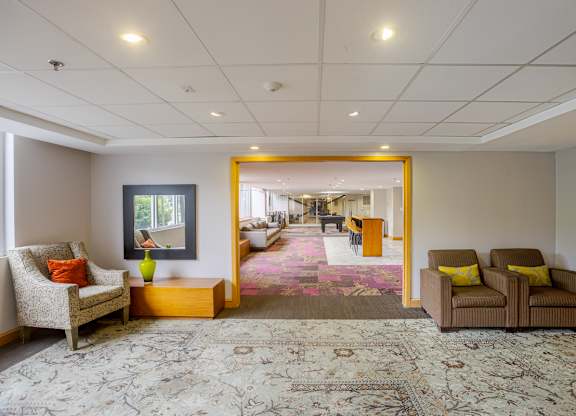 A living room with a rug, two chairs and a painting.