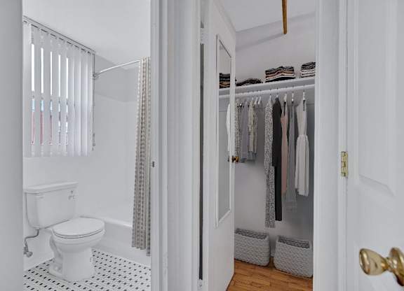 A white bathroom with a toilet, a shower with a curtain, and a closet with clothes.