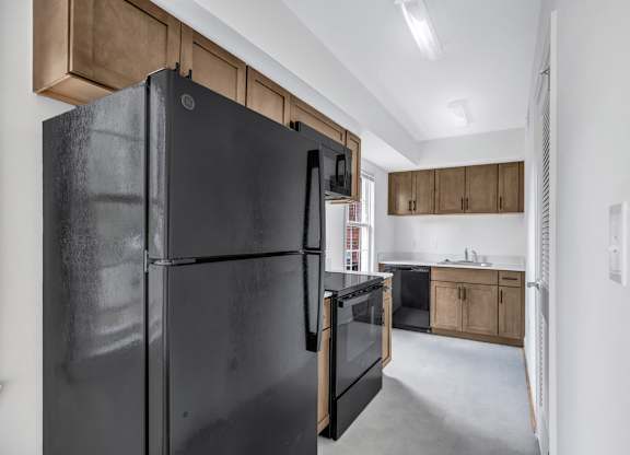 A black refrigerator stands in a kitchen with wooden cabinets and a white wall.