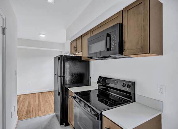 A black refrigerator and microwave are installed above a black stove in a kitchen with wooden cabinets.