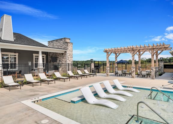 a swimming pool with chaise lounge chairs and a house in the background