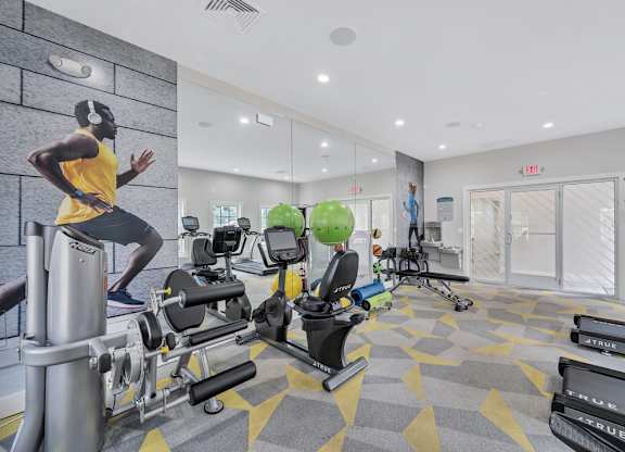a gym with cardio equipment and a man running on a treadmill
