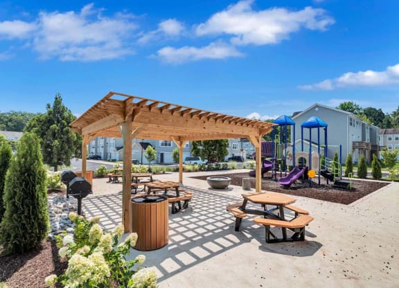 a picnic area with benches and tables and a playground in the background