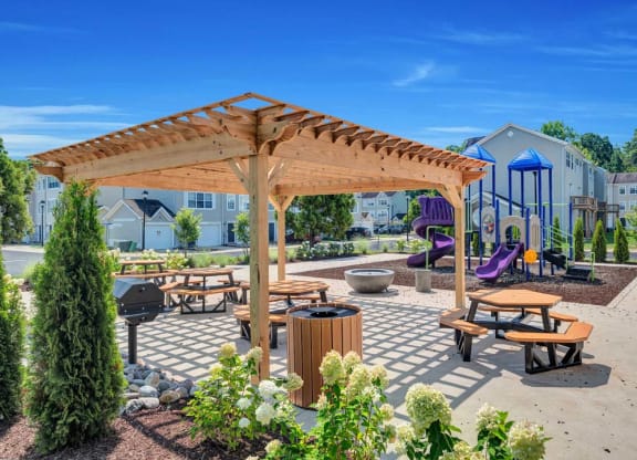 a picnic area with benches and tables with a playground in the background