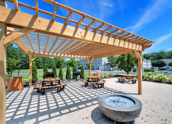 a fire pit and picnic tables under a wooden pergola with a blue sky in the