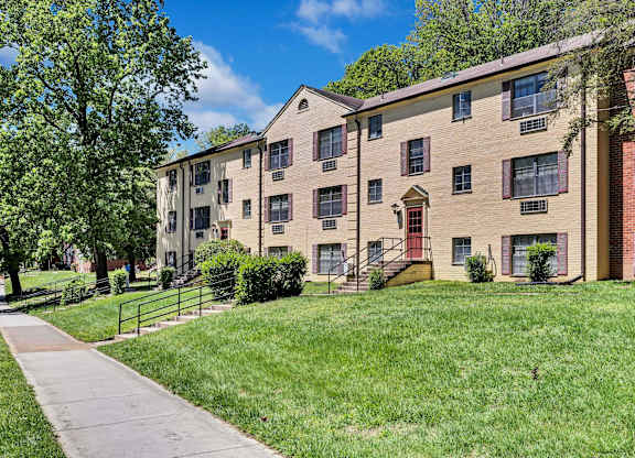 A brick apartment building with a red door and a green lawn in front.