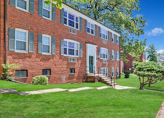 A red brick building with green shutters and a tree in front.