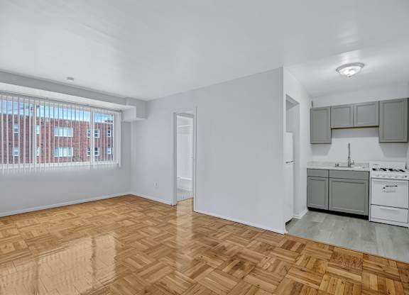 A room with wooden flooring and a kitchen area to the right.