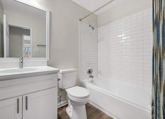 A bathroom with a white toilet and a shower with white subway tile backsplash curtain with a blue and brown pattern.