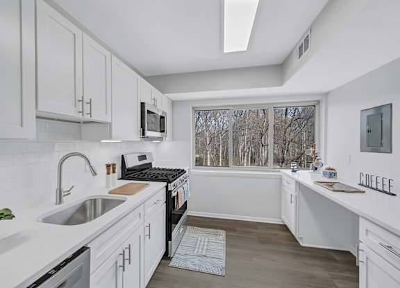 A kitchen with white cabinets and a window overlooking trees.