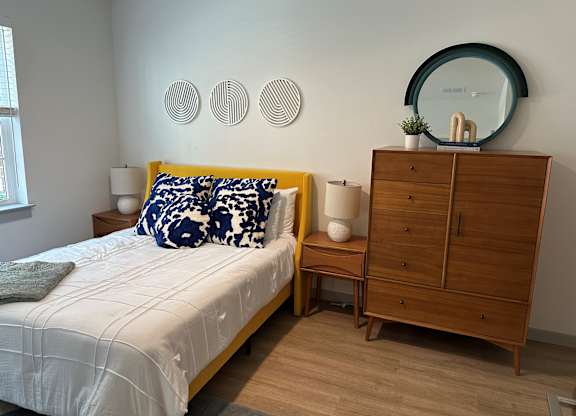 A bedroom with a bed, nightstand, and a dresser with a mirror on top.
