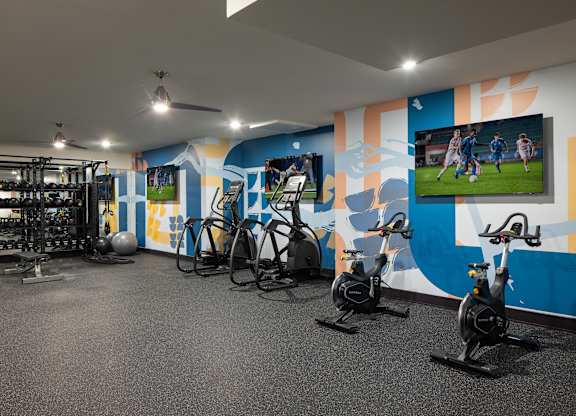 A gym with exercise bikes and a wall mural of a soccer game.