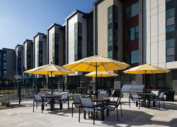 A patio with tables and chairs and umbrellas in front of a building.