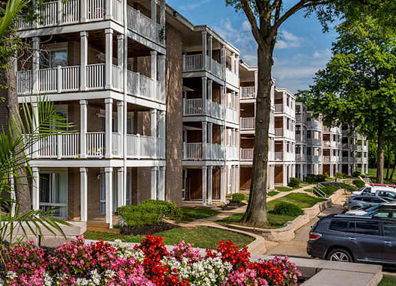a picture of an apartment complex with trees and flowers in the foreground