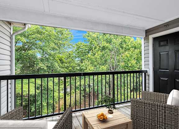 View from furnished balcony to lush wooded landscape.