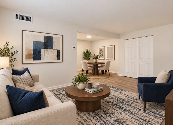 A living room with a beige couch, a blue armchair, a coffee table, and a painting on the wall.