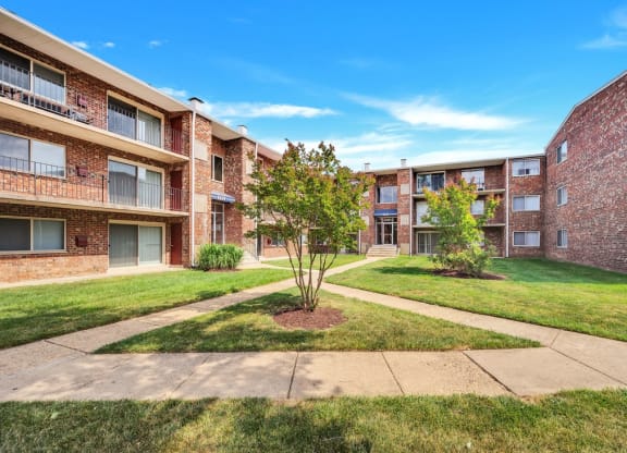 a grassy area with trees in front of an apartment building