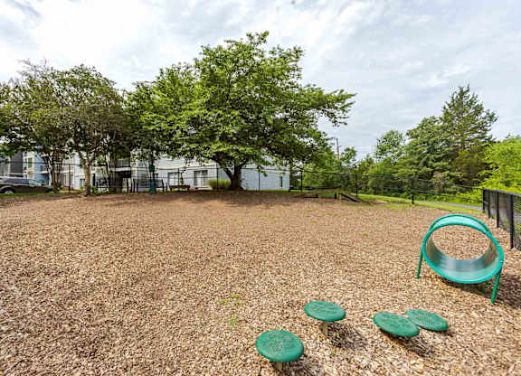 A playground with a green slide and three green plastic discs on a brown surface.