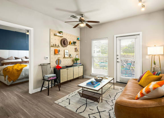 living room area with large couch and natural lighting from porch window/door. ceiling fans and peg board media wall with art and photos. bedroom viewable in background