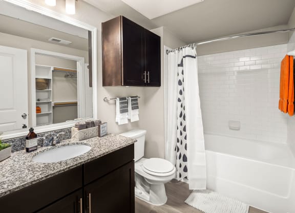 bathroom with matching countertops and cabinet above toilet. subway tile backsplash in shower/tub combo. Walk-in closet viewable from bathroom mirror.
