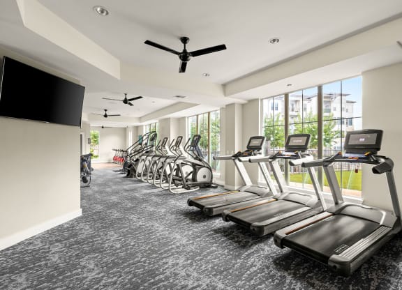 a gym with cardio machines and a tv
