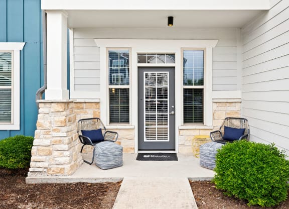 the front porch of a home with two chairs and a door