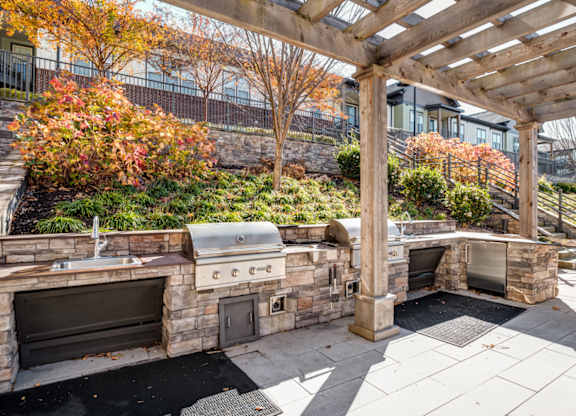 A stone patio with a grill and a pergola.