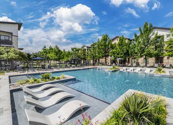 A pool surrounded by trees and a building in the background.