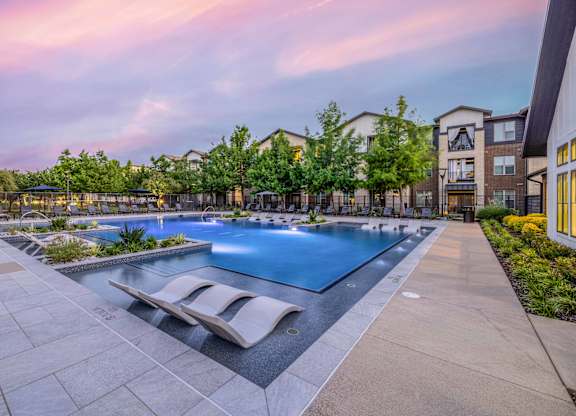 A swimming pool surrounded by a stone patio and lounge chairs.