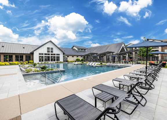 A pool area with sun loungers and a building in the background.