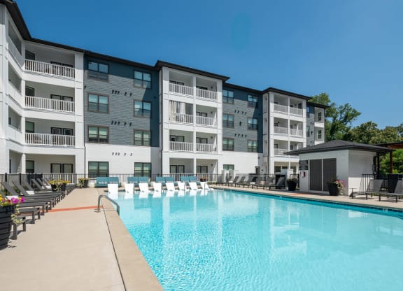 a swimming pool with lounge chairs and umbrellas in front of an apartment building