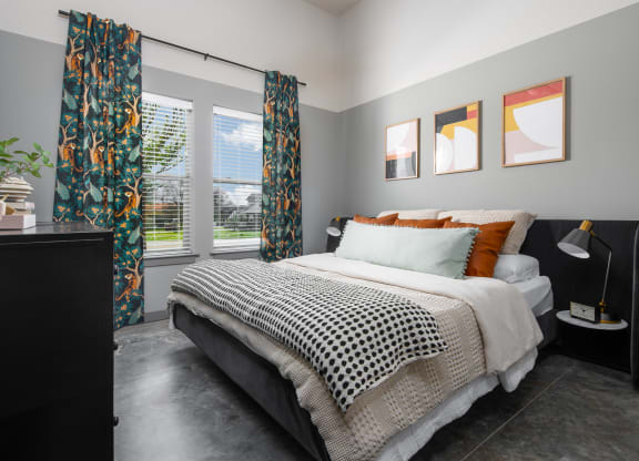 a bedroom with gray walls and a black and white bed with orange and black pillows