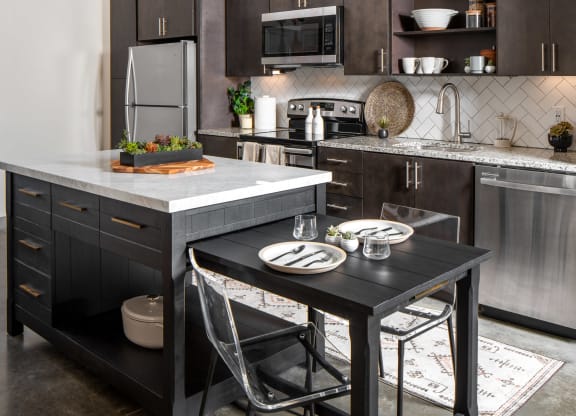 a kitchen with dark cabinets and a large island with a black table and two chairs